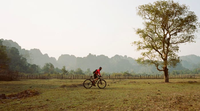 Rebecca cycling across a field in Laos. From the ride along the Ho Chin Minh Trail in 2015.